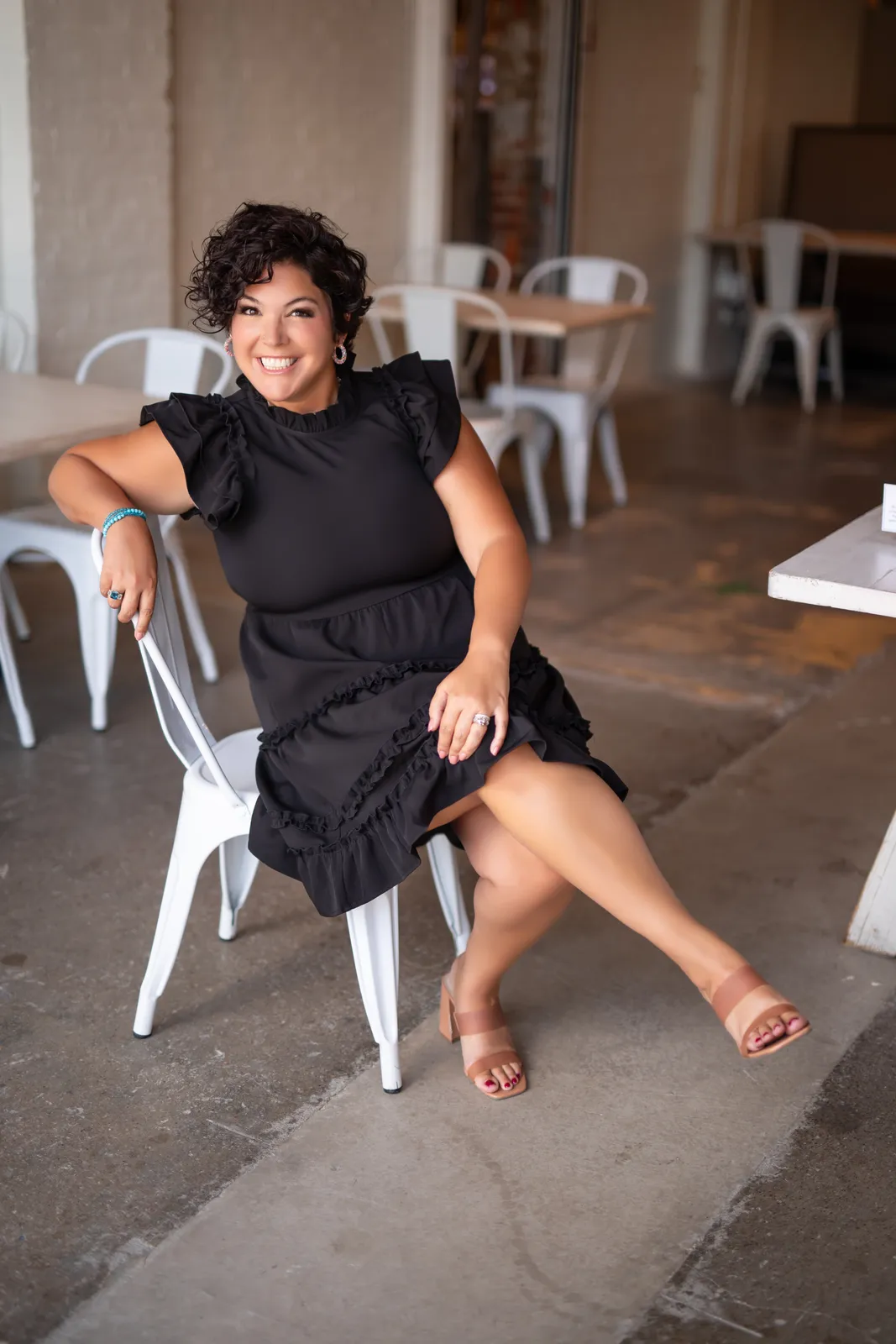 Jessica Doyle-Mekkes seated on a white chair in a black dress, smiling.