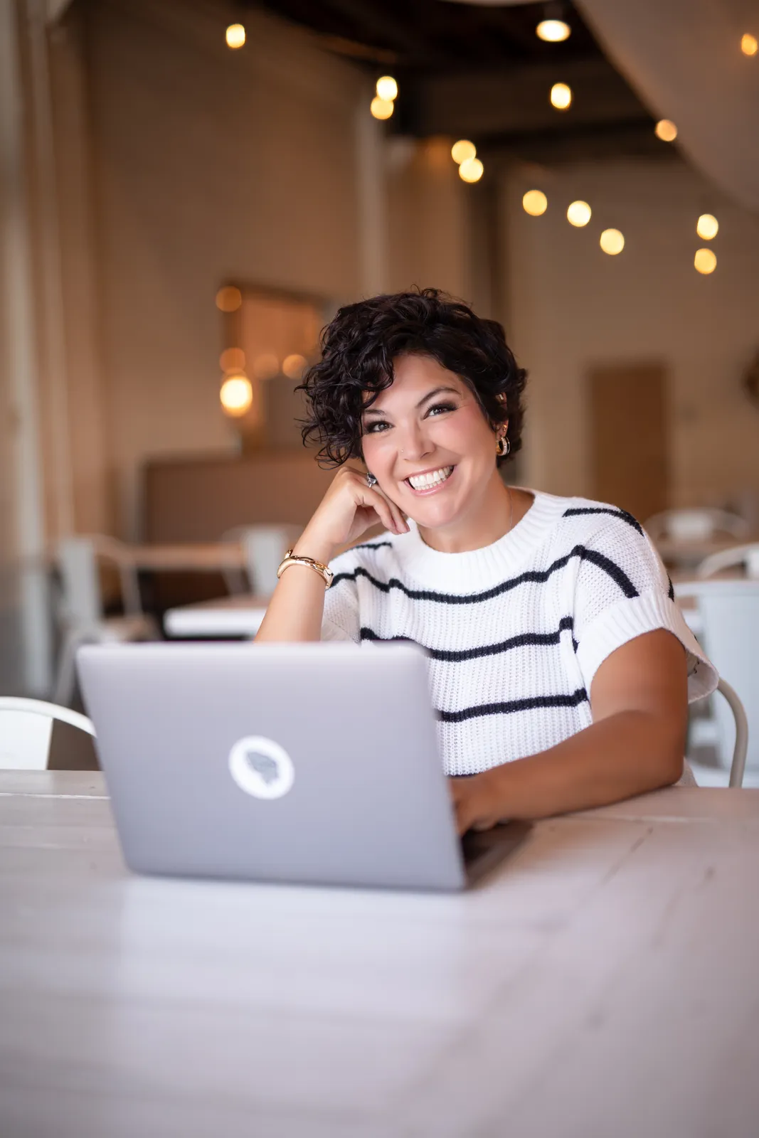 Jessica Doyle-Mekkes in a striped top at a laptop, chin on her hand, smiling.